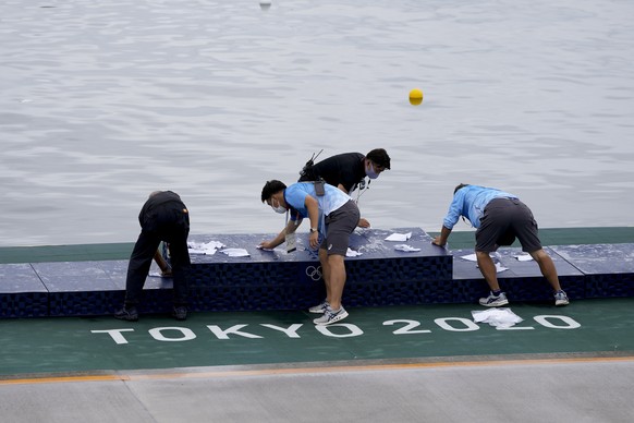 Olympic event volunteers dry off the medal podium after a rain in preparation for the canoe sprint medal ceremonies at the 2020 Summer Olympics, Saturday, Aug. 7, 2021, in Tokyo, Japan. (AP Photo/Lee  ...