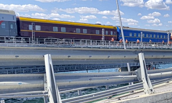 In this image from a video released on Wednesday, July 19, 2023 by the Russian National Antiterrorism Committee, A passenger train passes by the damaged parts of an automobile link of the Crimean Brid ...