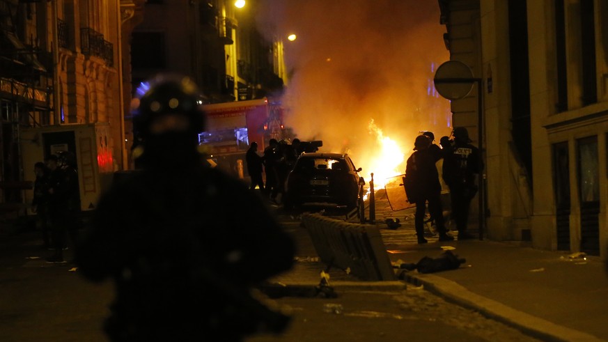 French police officers watch a car burning near the Champs-Elysee avenue following incidents after the Champions League soccer final match between PSG and Bayern Munich which is played in Lisbon, Port ...