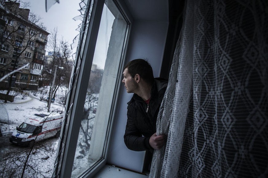 Krieg in Donezk: Mann schaut durch geborstene Fensterscheiben.
