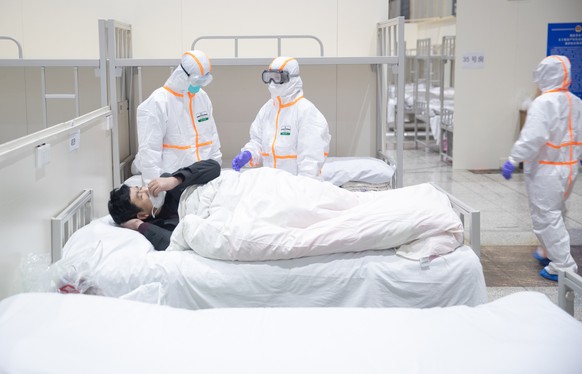 epa08196535 Medical staff attend to a patient infected by the coronavirus at a makeshift hospital at Wuhan International Convention and Exhibition Center in Wuhan City, Hubei Province, China, 05 Febru ...