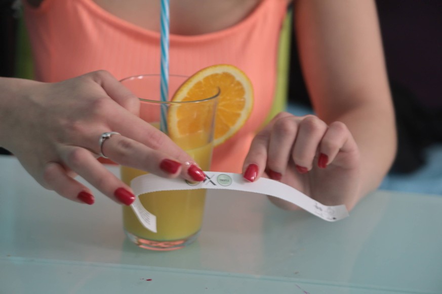 junge frau mit orangensaft und ko-tropfen-warnarmband testet den orangensaft junge frau mit orangensaft und ko-tropfen-warnarmband testet den orangensaft *** young woman with orange juice and ko drops ...