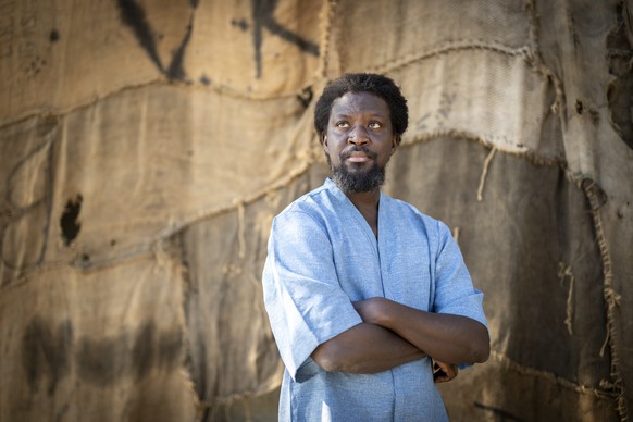 epa12067741 Ghanaian artist Ibrahim Mahama poses in front of his art installation made of recycled jute sacks from the cocoa trade, highlighting colonial legacies and global ties between Ghana and Swi ...
