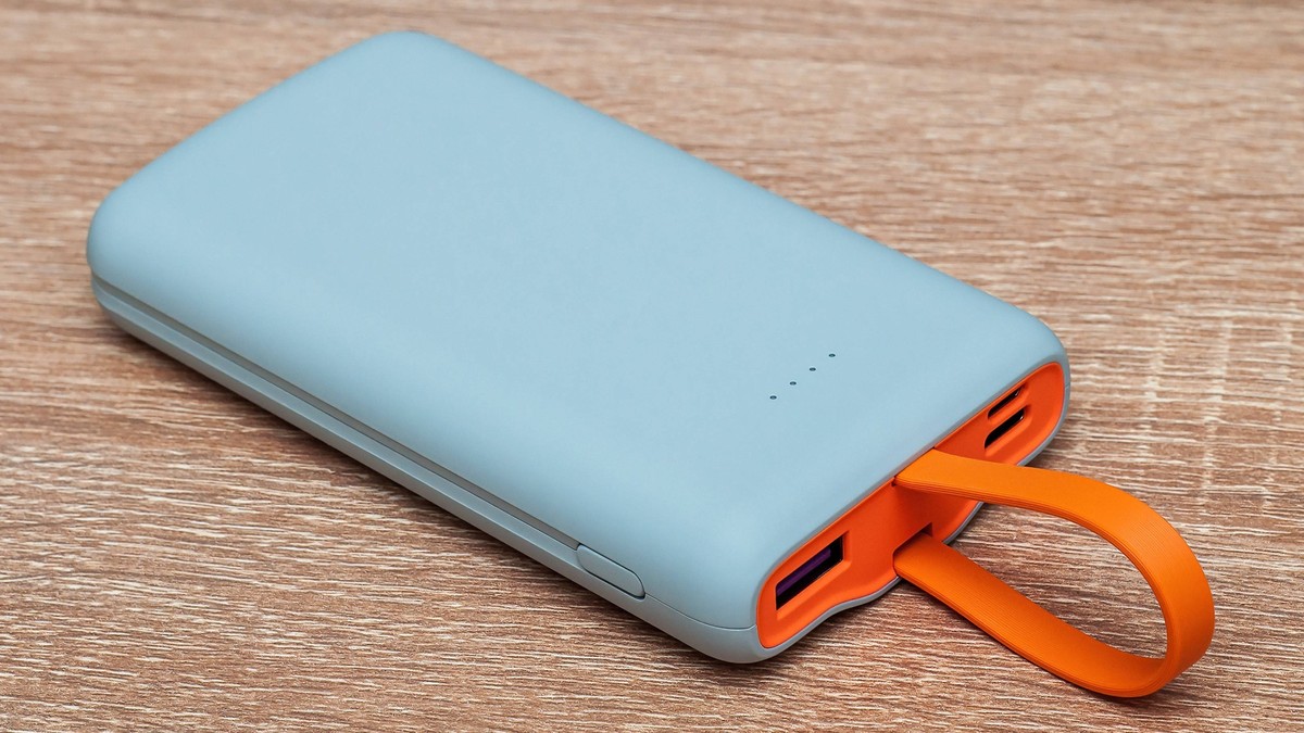 Ein modernes Gadget zum Aufladen von Geräten, eine Powerbank mit orangefarbenem USB-Griff auf einem hölzernen Hintergrund. Ein modernes Gadget zum Aufladen von Geräten, eine Powerbank mit orangefarben ...
