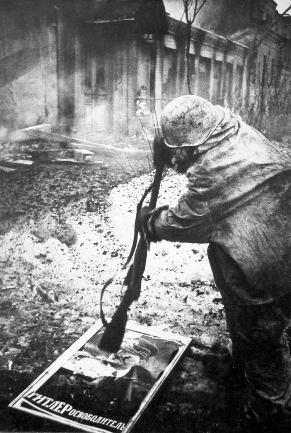 A Soviet soldier smashes a poster with the image of A. Hitler in liberated Gatchina with a rifle butt, January 1944