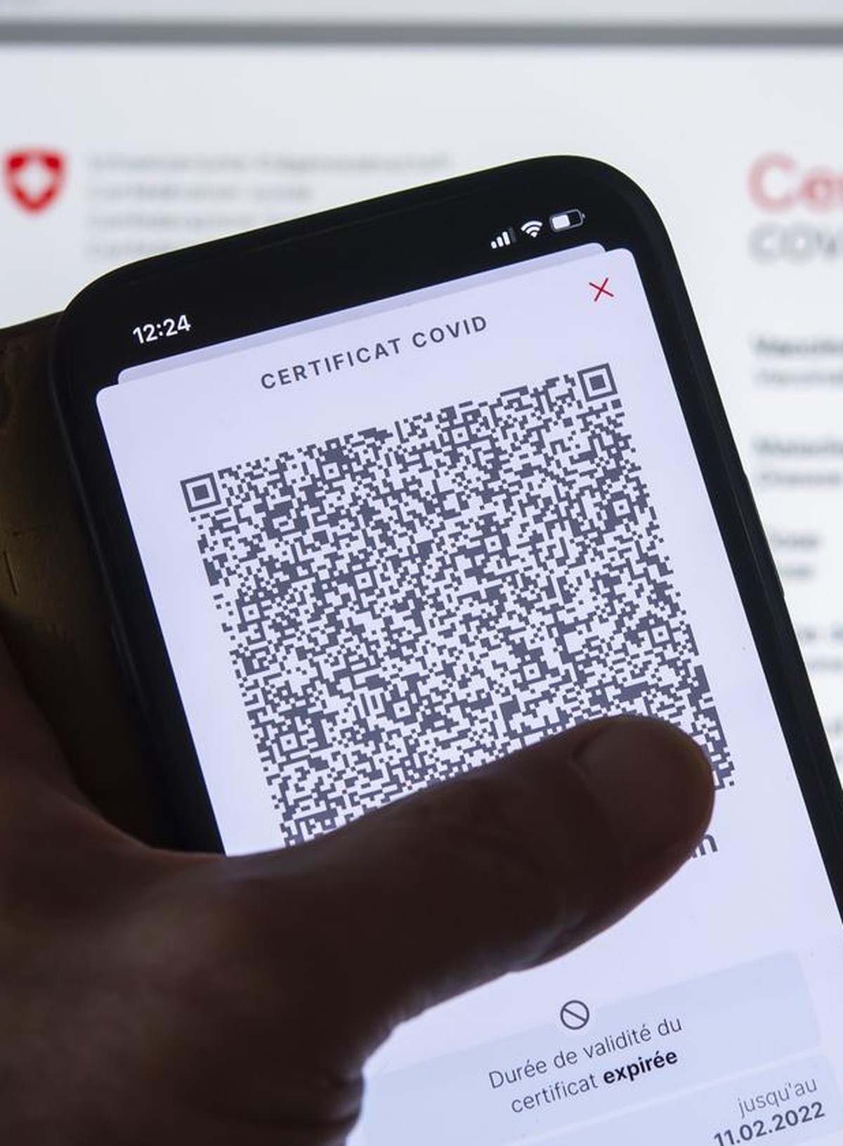 Une personne tient dans sa main un smartphone avec l'application Certificat Covid suisse et son code QR ou il est inscrit "Duree de validite du certificat expiree. Ce certificat ne repond pa ...