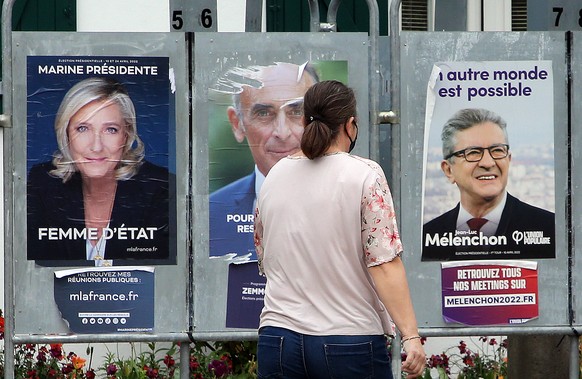 A woman walks past presidential campaign posters of French far-right presidential candidates Marine Le Pen and Eric Zemmour, and far-left leader Jean-Luc Melenchon, right, in Anglet, southwestern Fran ...