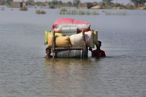 Flood-affected people use cot to salvage belongings from their nearby flooded home caused by heavy rain, in Qambar Shahdadkot district of Sindh Province, of Pakistan, Friday, Sep. 2, 2022. Planes carr ...