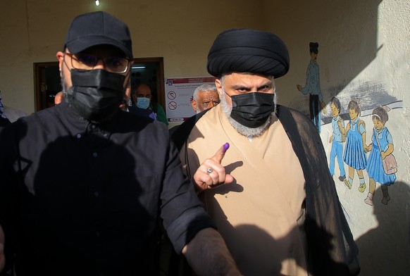 Populist Shiite cleric Muqtada al-Sadr, right, displays his ink-stained finger that shows he voted, at a polling center during the parliamentary elections in Najaf, Iraq, Sunday, Oct. 10, 2021. Iraq c ...