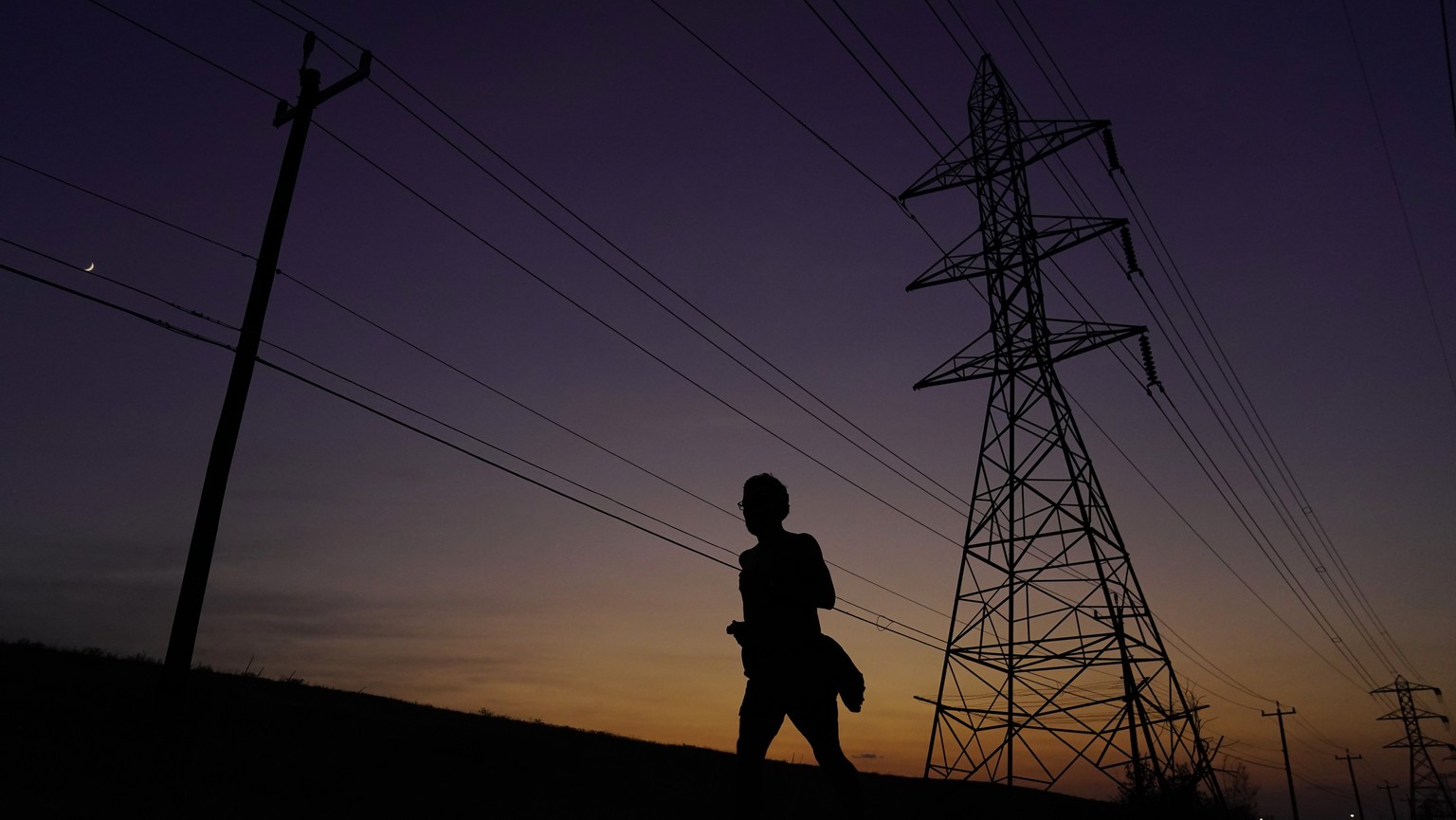 FILE - A jogger passes power lines during a sunset run, Aug. 20, 2023, in San Antonio, as high temperatures continue to stress the power grid. On Thursday, Sept. 7, Texas&#039; power grid manager agai ...