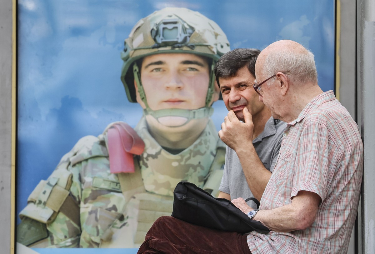 epa12258819 Two men sit on a bench in front of an advertisement for military conscription featuring a portrait of a Russian soldier at a bus stop in Moscow, Russia, 24 July 2025, as troops are deploye ...
