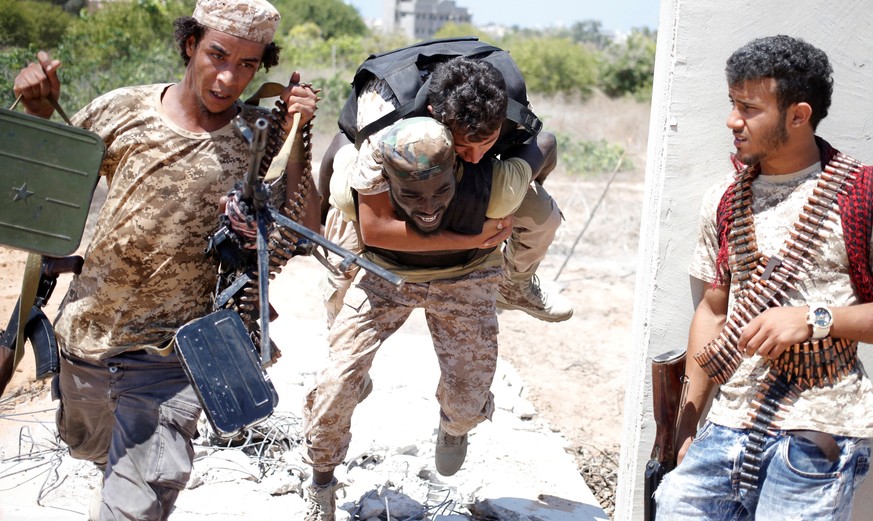 A fighter of Libyan forces allied with the U.N.-backed government runs for cover with another fighter while carrying a wounded fighter during a battle with Islamic State fighters in Sirte, Libya, July ...