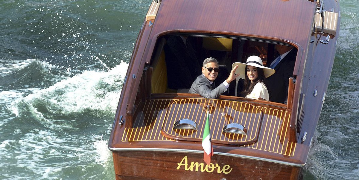George Clooney, flanked by his wife Amal Alamuddin, waves from a water-taxi after leaving the city hall in Venice, Italy, Monday, Sept. 29, 2014. George Clooney married human rights lawyer Amal Alamud ...