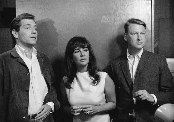 FILE - Elizabeth Taylor is flanked by actor George Segal, left, a co-star in “Who’s Afraid of Virginia Woolf?” and Mike Nichols director of the film, as they watched preparation in this Oct. 20, 1965  ...