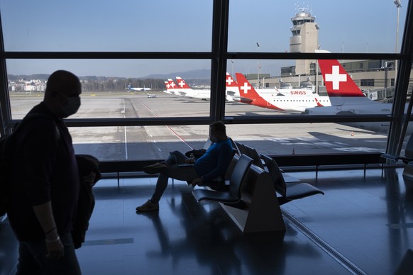 Passengers wearing a face mask wait before boarding in an airplane in front of parked Swiss International Air Lines airplanes at the Zuerich Airport (Flughafen Zuerich) during the coronavirus disease  ...