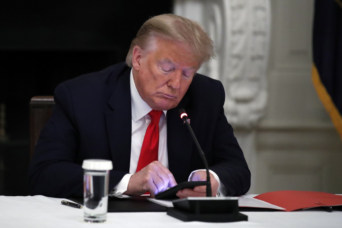 FILE - President Donald Trump looks at his phone during a roundtable with governors on the reopening of America's small businesses, in the State Dining Room of the White House in Washington, June ...