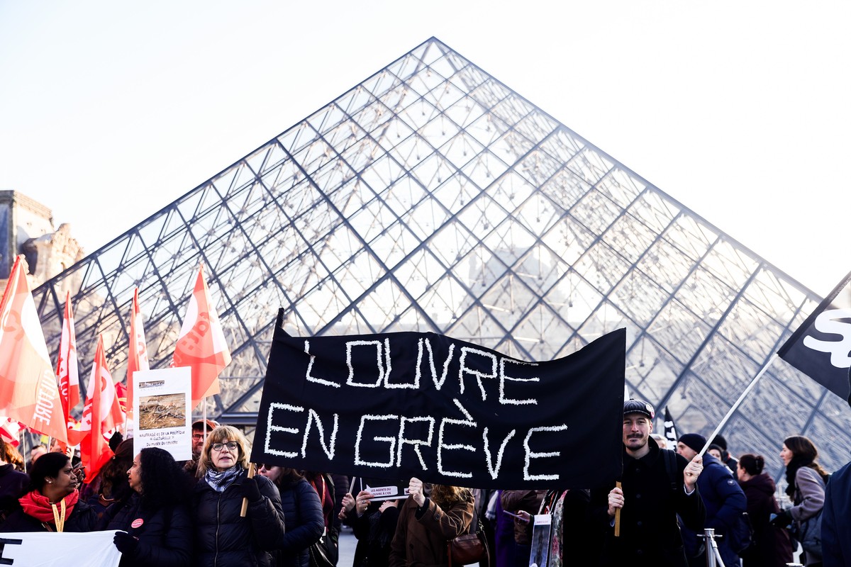 epa12593793 Louvre workers from various unions, including CGT, CFDT, and SUD, hold a banner reading 'Louvre on strike' during a demonstration in front of the museums pyramid on the first da ...