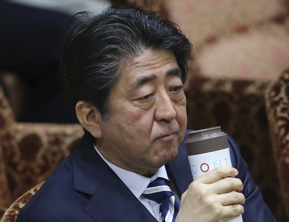 Japanese Prime Minister Shinzo Abe holds a bottle of a drink during a meeting of the upper house budget committee at the parliament in Tokyo, Monday, March 19, 2018. Support ratings for Abe have plung ...