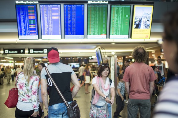 Menschen schauen auf die Anzeigetafeln am Flughafen, aufgenommen am Samstag, 25. Juli 2015, in Zuerich. (KEYSTONE/Ennio Leanza)