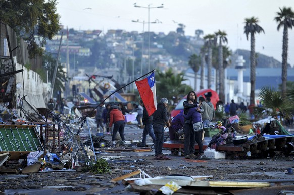 A couple embraces in the middle of a debris strewn street, where a Chilean flag was placed after an earthquake-triggered tsunami hit Coquimbo, Chile, Thursday, Sept. 17, 2015. Several coastal towns we ...