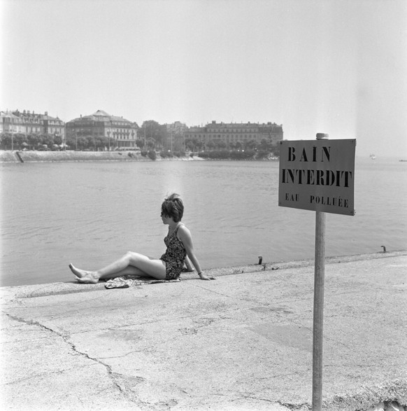 Eine Badeverbotstafel und eine Frau im Badekleid am verschmutzten Neuenburgersee, aufgenommen im Sommer 1964. (KEYSTONE/Str)