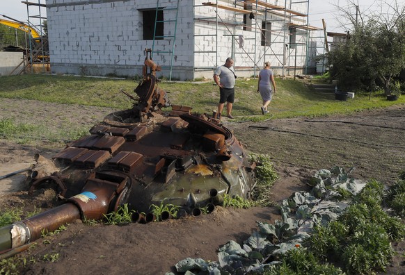 epa10734035 Valeriy and Yulia walk past the remains of a Russian tank in the garden near their home at the village of Velyka Dymerka, Kyiv region, Ukraine, 05 July 2023 (issued 08 July 2023). Valeriy  ...