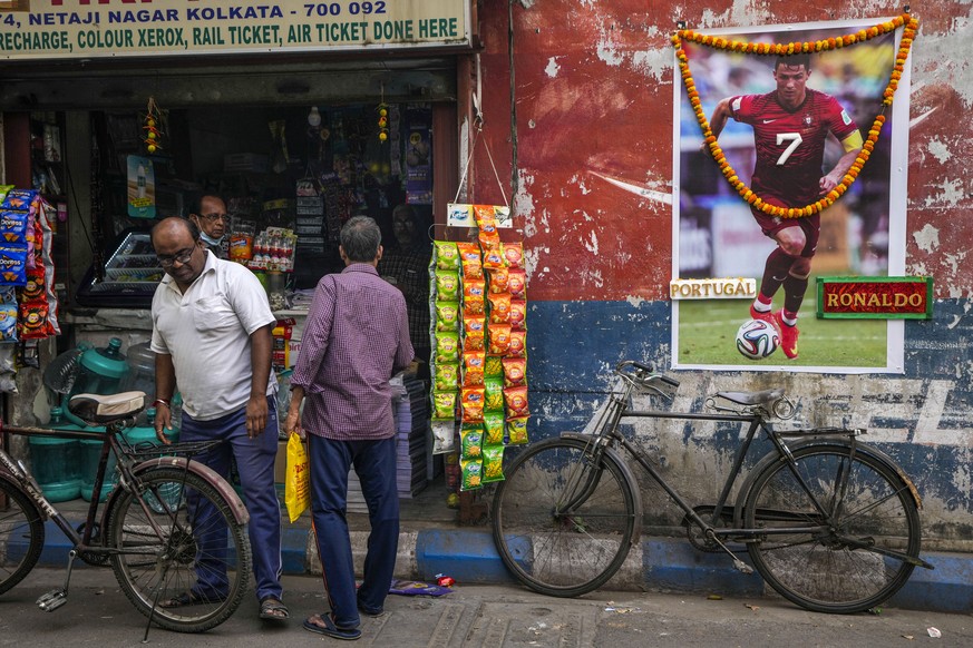 People buy grocery from a shop next to a garlanded photograph of Portugal&#039;s Cristiano Ronaldo put up by fans to mark the ongoing soccer World Cup in Kolkata, India, Thursday, Dec. 8, 2022. (AP Ph ...