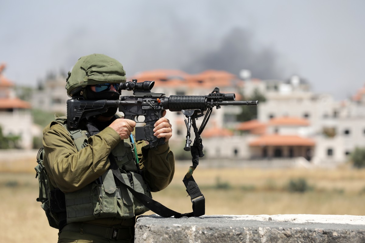 epa10703679 An Israeli soldier stands guard as smoke rises from the Palestinian town Turmus Aya, next to the Israeli settlement of Eli in the West Bank, 21 June 2023. Four people were killed in a Pale ...