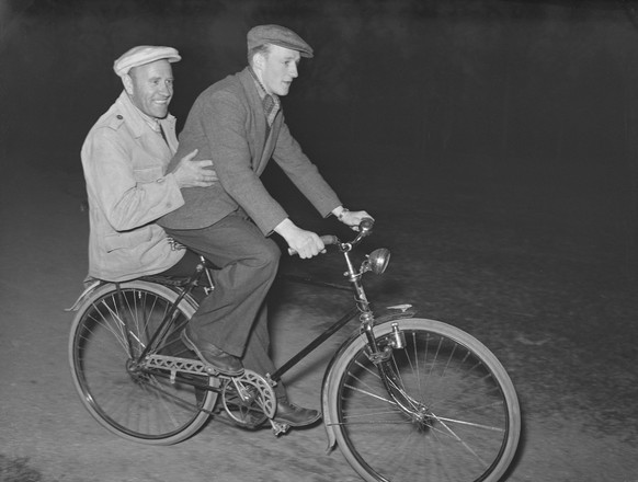 Frau aus den 1940er Jahren auf einem Fahrrad. Die schwedische Schauspielerin Viveca Lindfors ist dabei, ihr Fahrrad zu reparieren. Man beachte die Sandsäcke vor dem Wohnhaus und den Eingang zum Keller ...