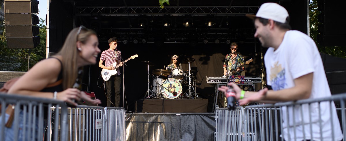 epaselect epa08575327 Two festival goers talk about the separation of the two visitor areas during the soundcheck of the Swiss band Hot Like Sushi, at the 'Swiss Mountain Roadshow', during t ...