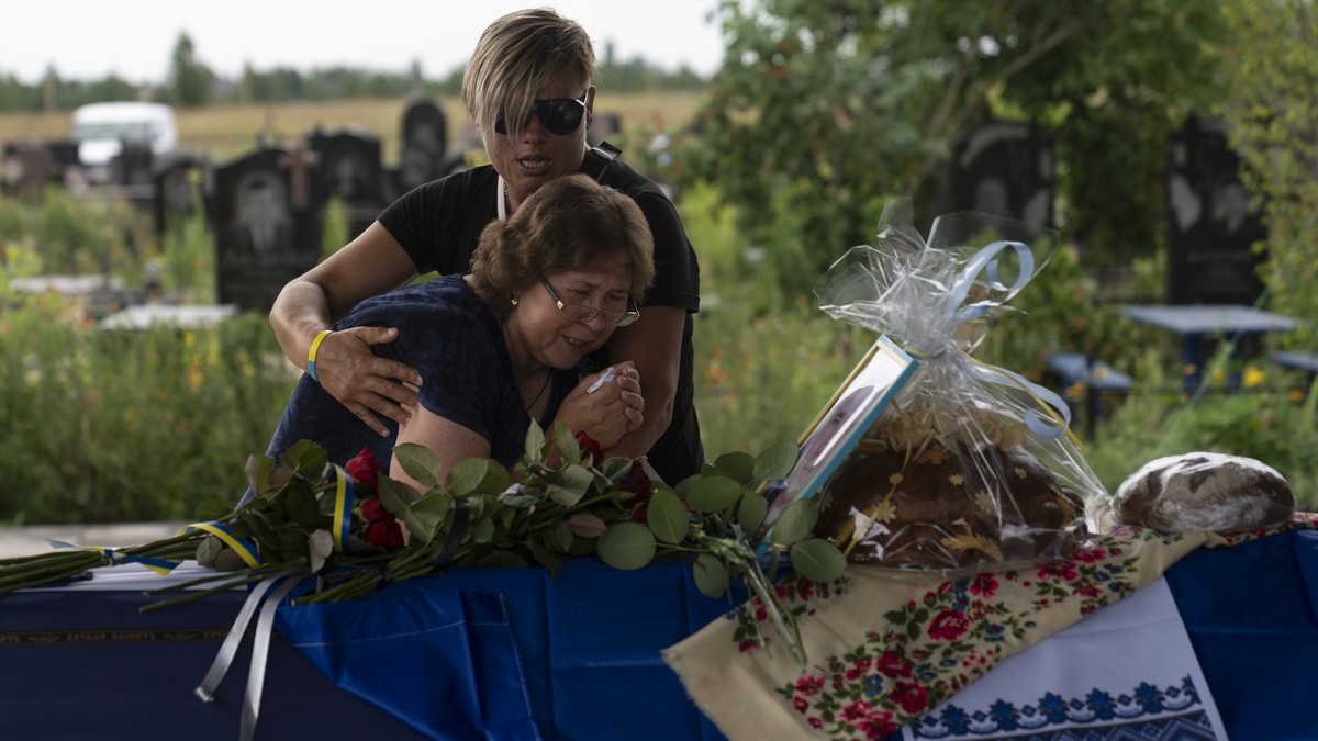 Comforted by Khrystyna Liubymska, top, Zynaida Nedoleshko weeps next to a casket carrying the remains of her nephew, Roman Shadlovskyi, during a reburial service for him in Bucha, Ukraine, Tuesday, Ju ...