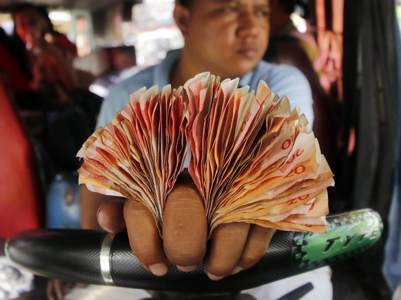 epa06387631 A Filipino driver holds his earnings on his fingers as he drives a jeepney, a popular and uniquely Filipino mode of mass transport, along a street in Paranaque city, south of Manila, Phili ...