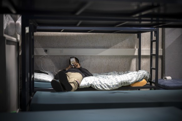 Ein Mann benutzt sein Mobiltelefon waehrend er in einem Schlafsaal auf einem Bett liegt, aufgenommen waehrend eines Medienrundgans im Bundesasylzentrum Zuerich, am Donnerstag, 27. Oktober 2022 in Zuer ...