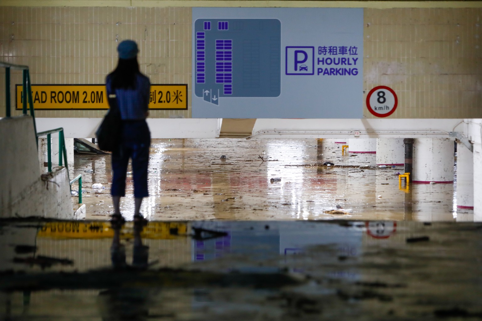 epa10847601 A woman stands in front of the entrance to a flooded car park following continued torrential rains hitting the city, in Hong Kong, China, 08 September 2023. The government has stopped scho ...