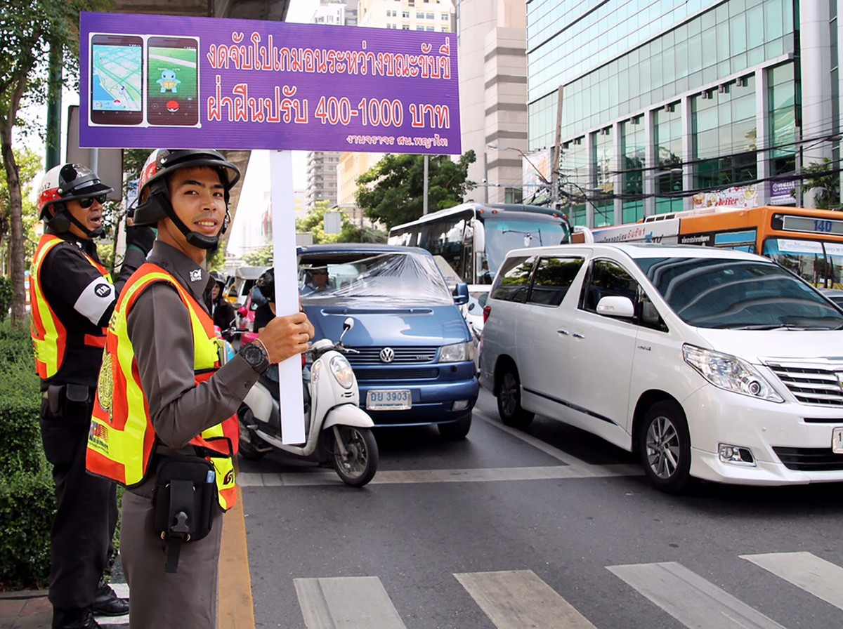 epa05506563 A Thai traffic policeman holds a banner reading 'No Pokemon Go while driving, violators will be fined' during the 'Pokemon Traffic No Go' campaign at a busy street in B ...