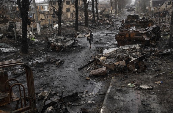 A woman navigates a debris-filled street where destroyed Russian military vehicles stand in Bucha on the outskirts of Kyiv, Ukraine, Sunday, April 3, 2022. (AP Photo/Rodrigo Abd)