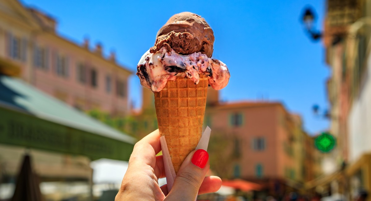 Woman s hand holding artisanal chocolate gelato in a cone, view of traditional colorful houses in the Old Town Vieille Ville of Menton South of France Model Released Property Released xkwx artisanal a ...