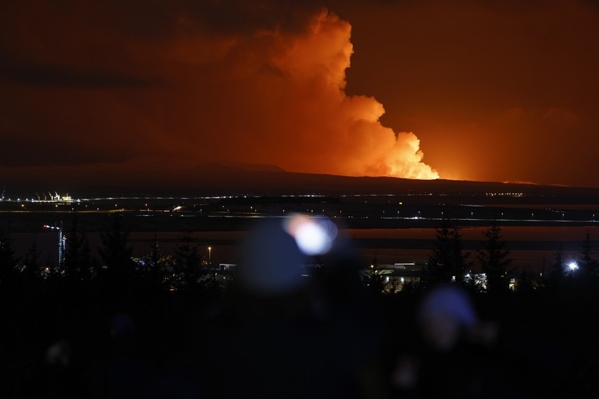 People watch as the night sky is illuminated caused by the eruption of a volcano on the Reykjanes peninsula of south-west Iceland seen from the capital city of Reykjavik, Monday Dec. 18, 2023. (AP Pho ...