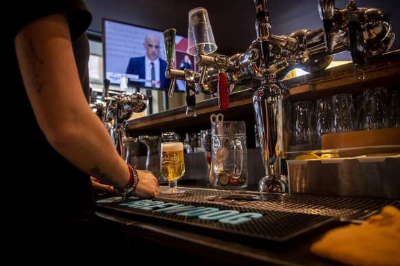 A waitress is preparing a beer wearing a protective mask while watching on a TV screen Swiss Interior and Health Minister Alain Berset as he speaks during a press conference in Bern announcing new mea ...