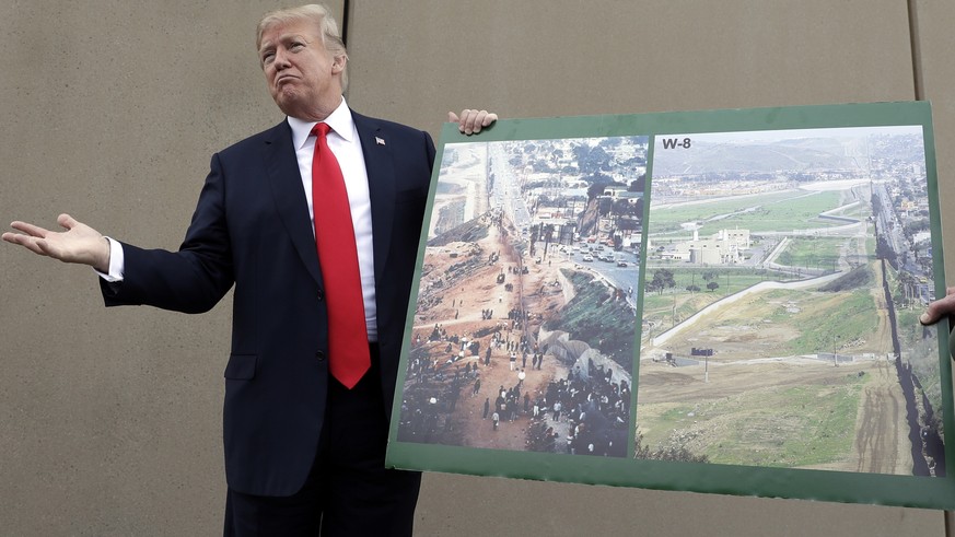 FILE - In this Tuesday, March 13, 2018, file photo, President Donald Trump holds a poster with photographs of the U.S. - Mexico border area as he reviews border wall prototypes in San Diego with Rodne ...
