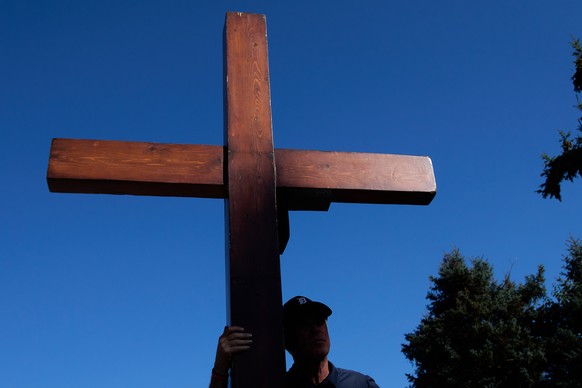 Dan Beazley, of Northville, carries a homemade cross to The Church of Jesus Christ of Latter-day Saints in Grand Blanc Township, Mich., Tuesday, Sept. 30, 2025, after a man rammed his vehicle into the ...