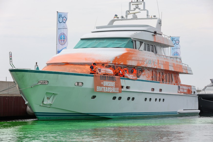 dpatopbilder - 20.06.2023, Schleswig-Holstein, Neustadt in Holstein: Teilnehmer einer Protestaktion stehen mit Transparenten auf einer Yacht im Hafen von Neustadt. Auf einem Transparent ist die Aufsch ...