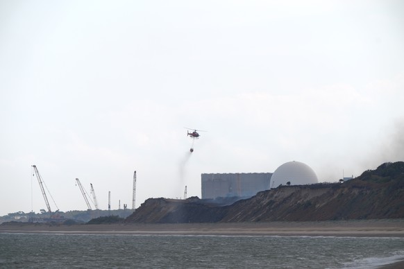 A helicopter flies water collected from the sea to drop on the wildfire at Dunwich Heath, near Leiston, close to the Sizewell B nuclear power station, where a major incident has been declared as firef ...