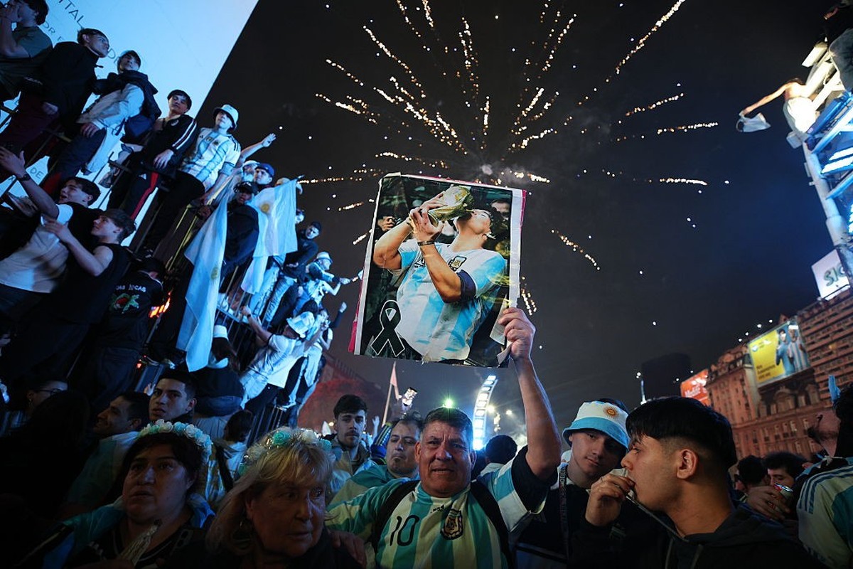 BUENOS AIRES, ARGENTINA - JULY 15: A fan of Argentina raises an image of Diego Maradona as fireworks light in the background during the celebrations after their team's victory in the FIFA World C ...