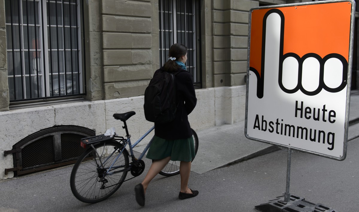 Une personne passe devant un panneau "Heute Abstimmung" lors d'une votation federal ce dimanche 8 mars 2015 a Fribourg. Le peuple Suisse doit se prononcer sur deux initiatives populaire ...