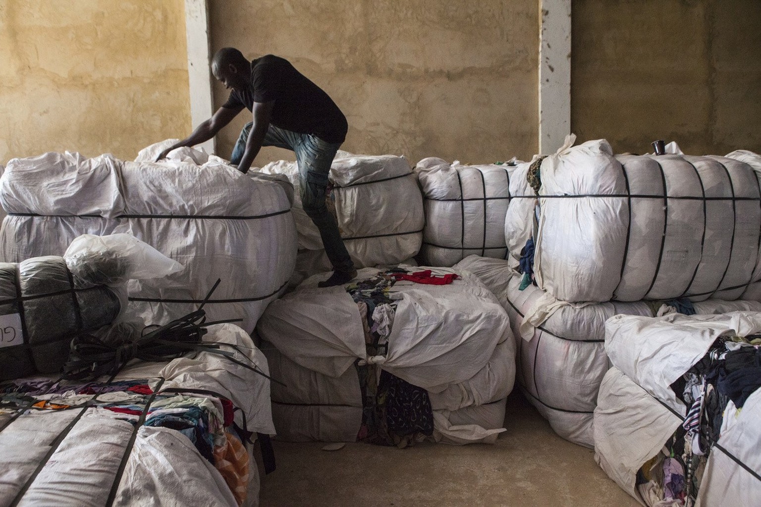 In this photo taken Monday, Oct. 24, 2016, a worker climbs on top of bulk secondhand clothing imported from Italy at the the Invotex warehouse in Dakar, Senegal. Secondhand T-shirts, jeans and dresses ...