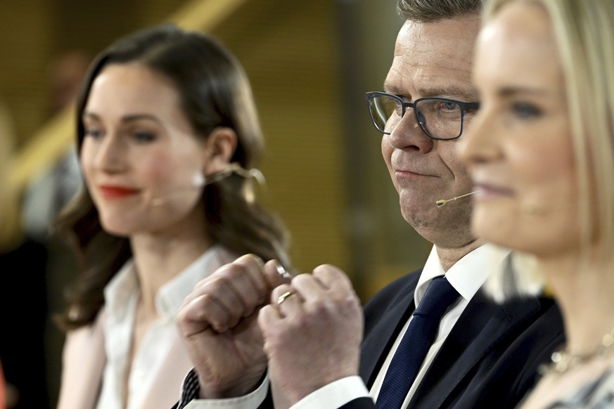 Chair of SDP Sanna Marin, left, and chair of The Finns party Riikka Purra, right, look on as National Coalition Party chair Petteri Orpo cheers at the Finnish parliamentary elections media reception a ...