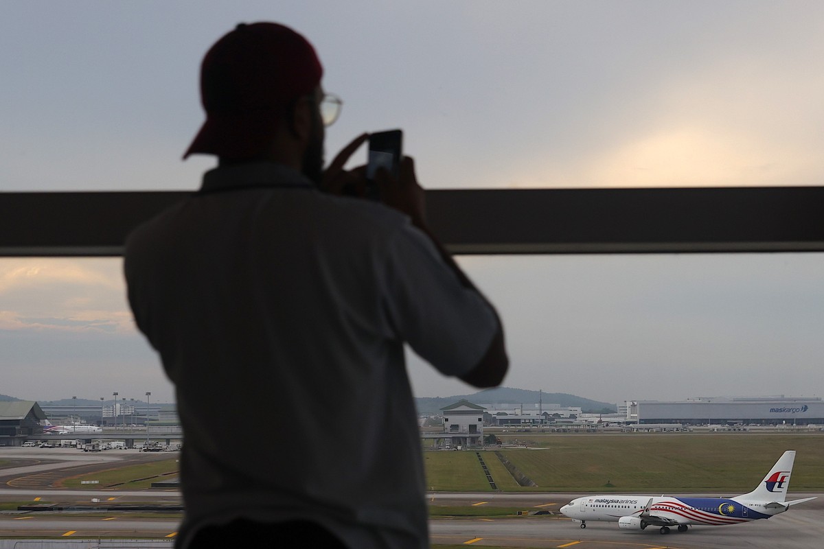 epa11948243 A visitor takes a picture of a Malaysia Airlines aircraft at the Kuala Lumpur International Airport, on the 11th anniversary of missing Malaysia airlines MH370 in Sepang, outside Kuala Lum ...