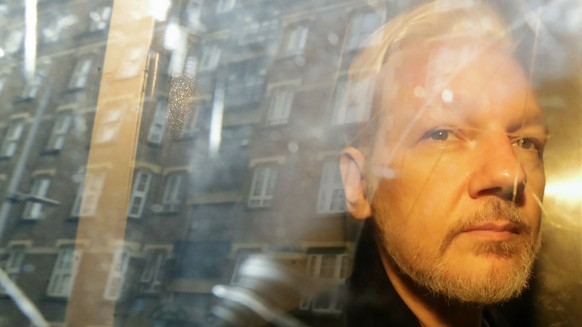 FILE - In this Wednesday May 1, 2019 file photo, buildings are reflected in the window as WikiLeaks founder Julian Assange is taken from court, where he appeared on charges of jumping British bail sev ...