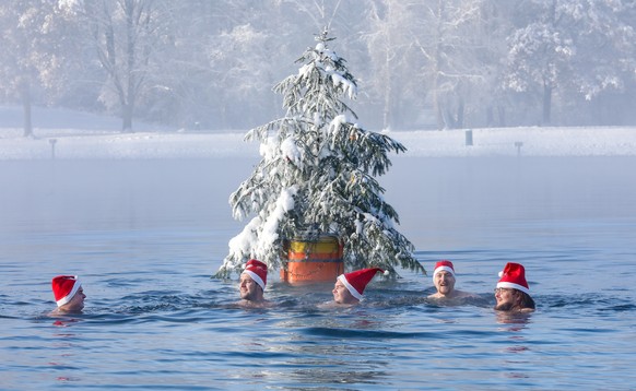 dpatopbilder - 11.12.2022, Baden-W�rttemberg, Ertingen: M�nner mit Nikolausm�tzen schwimmen bei Minusgraden im Schwarzachtalsee um einen Weihnachtsbaum auf einer Boje herum. Foto: Thomas Warnack/dpa + ...